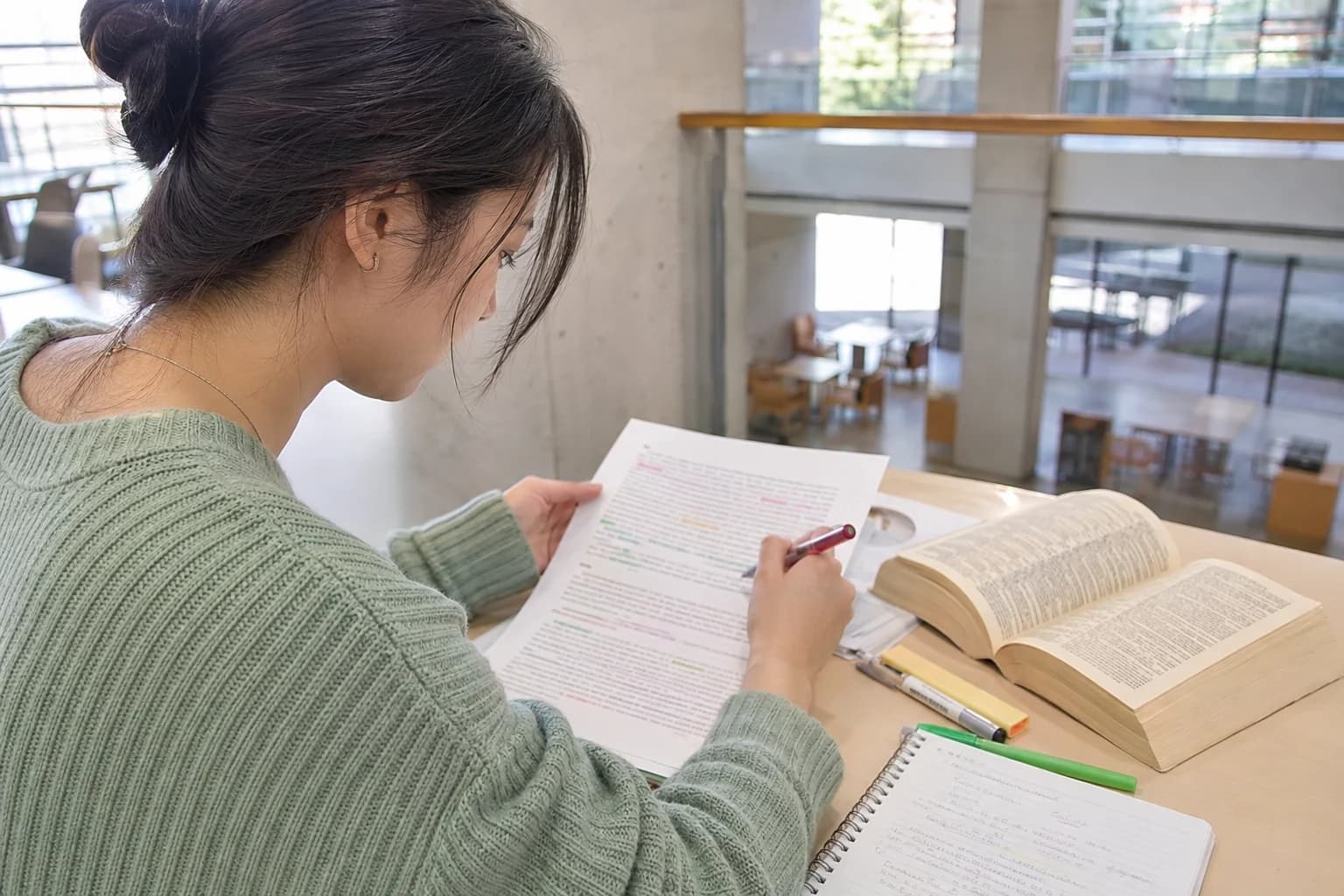 Student color coding grammar changes in her own English paragraph beside a reference book